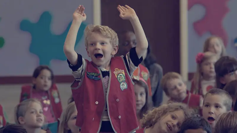 An excited boy in an AWANA vest raising his arms with other children