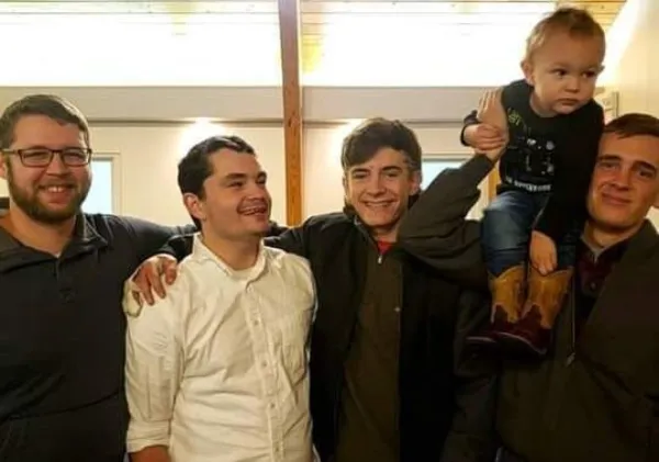 A group of young men smiling together, one holding a toddler